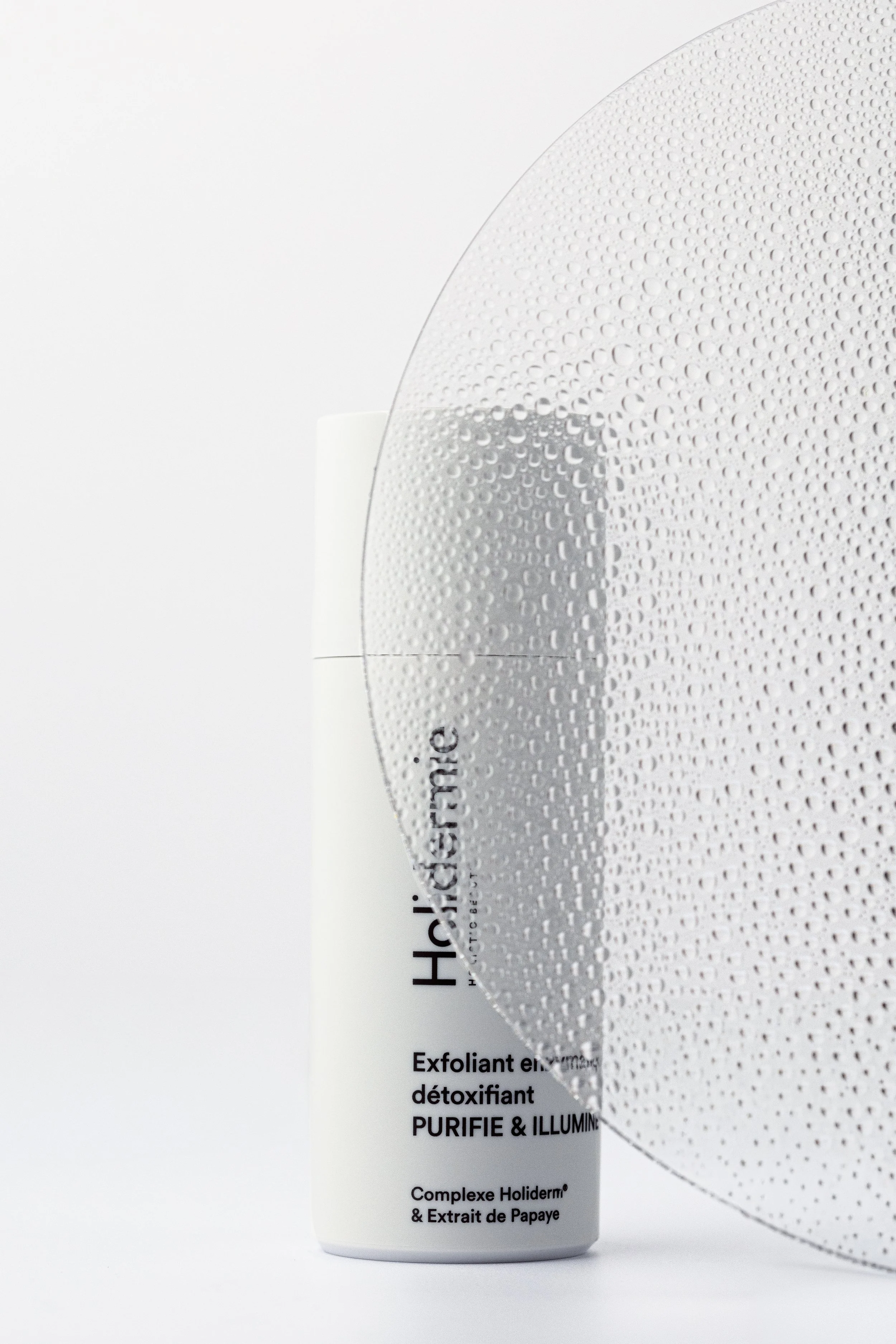 Holidermie skincare product photographed behind a textured transparent surface in a clean minimalist composition.