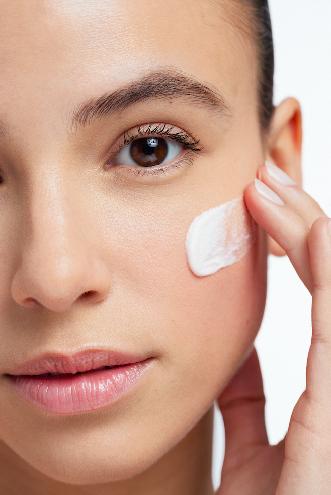 Beauty close-up of a woman applying white skincare cream to her cheek. Beauty image with colourful circles