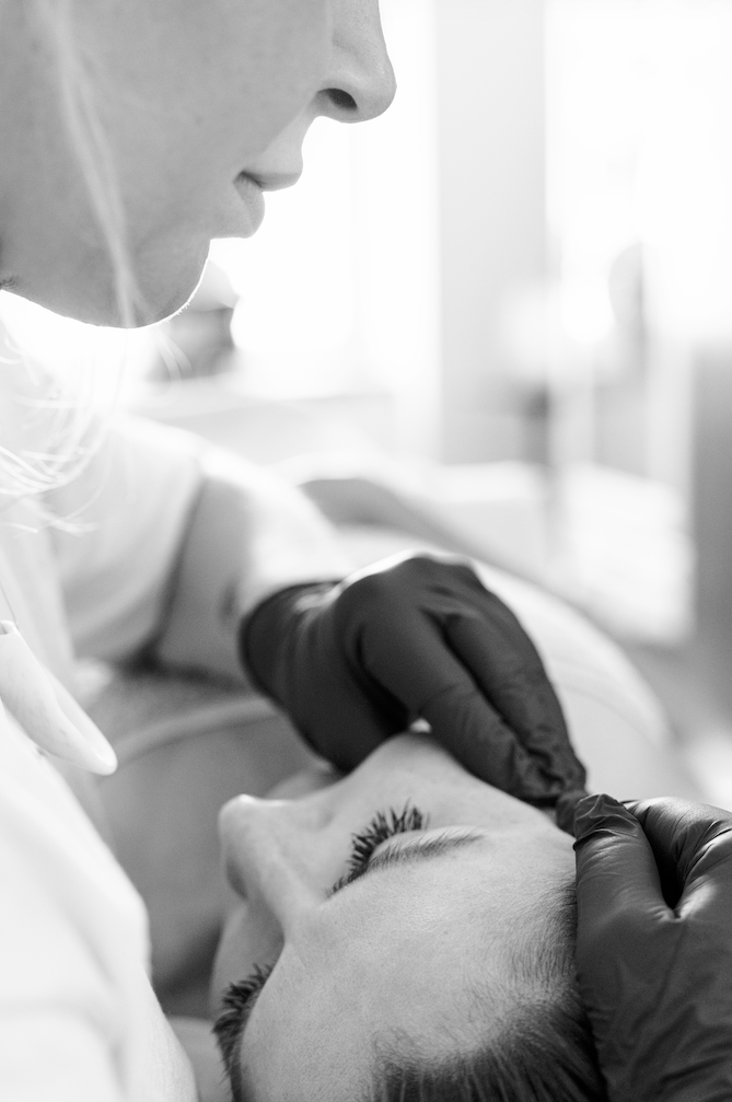 Black and white close-up of a professional beauty treatment being performed on a woman's face.