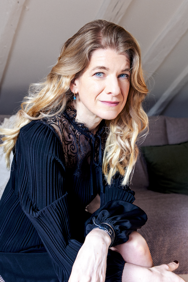 Intimate portrait of a blonde woman in a dark blouse photographed at home in Paris.