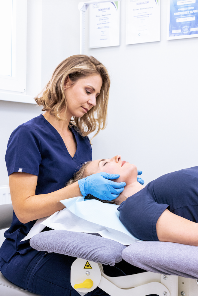 Female practitioner in blue scrubs performing a facial treatment in a professional wellness clinic.