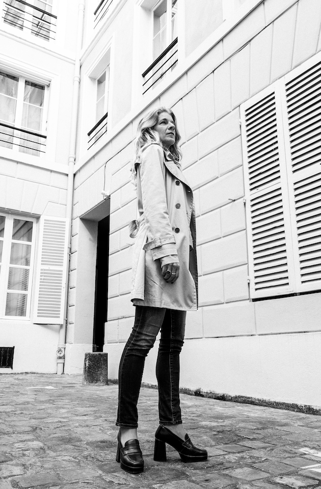 Black and white environmental portrait of a woman standing in a Paris courtyard.