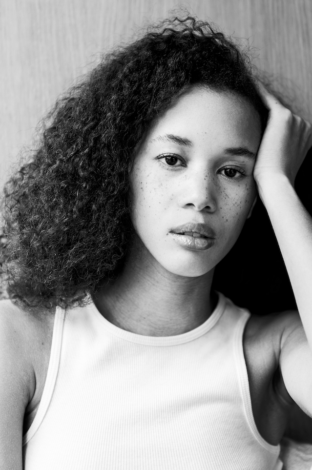Black and white close-up portrait of a woman with curly hair in natural light.