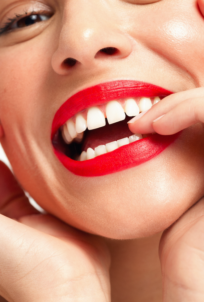 Close-up beauty photograph of a smiling mouth with glossy bright red lipstick.
