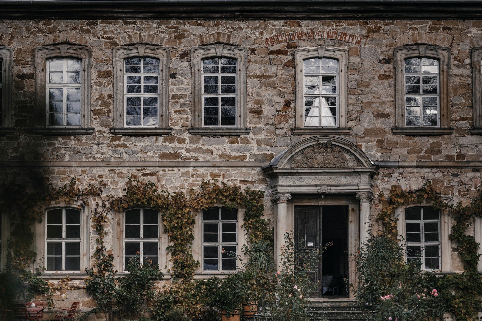 Alte Steindekorierte Villa mit mehreren Fenstern und einer Tür im Jugendstil, umgeben von Gartenpflanzen.
