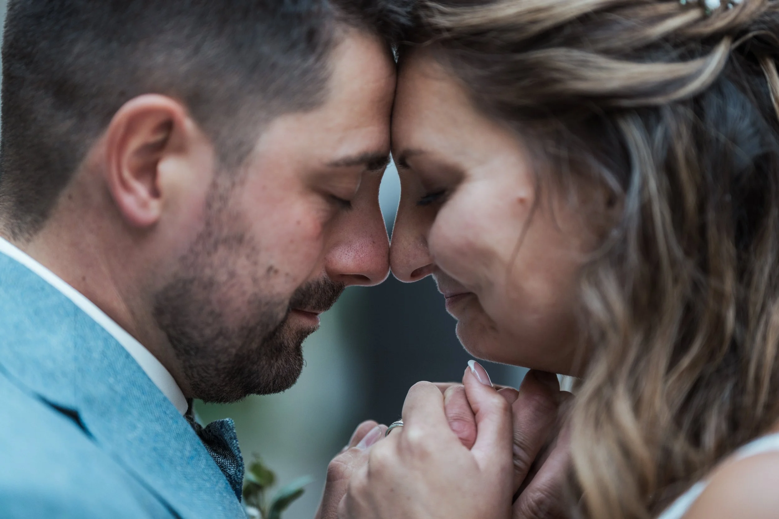 Ein Brautpaar mit verschränkten Händen, das sich mit ihren Stirnen berührt, in einem intimen Moment bei ihrer Hochzeit.