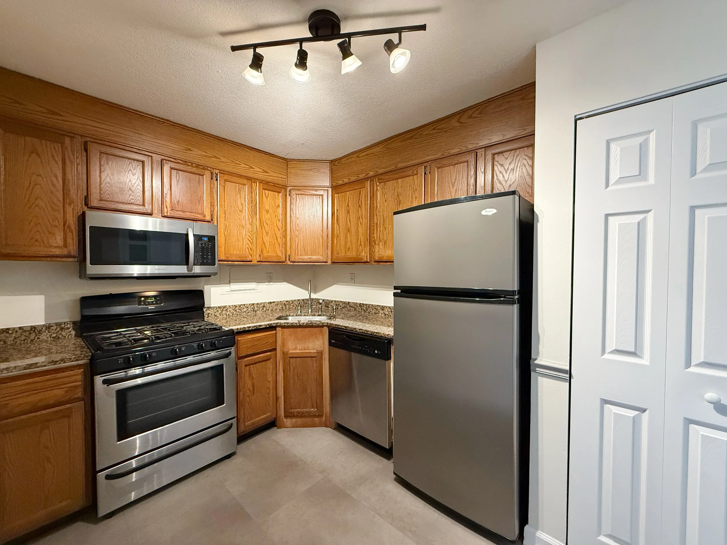 Kitchen with wooden cabinets, stainless steel microwave, stove, refrigerator, and granite countertops.