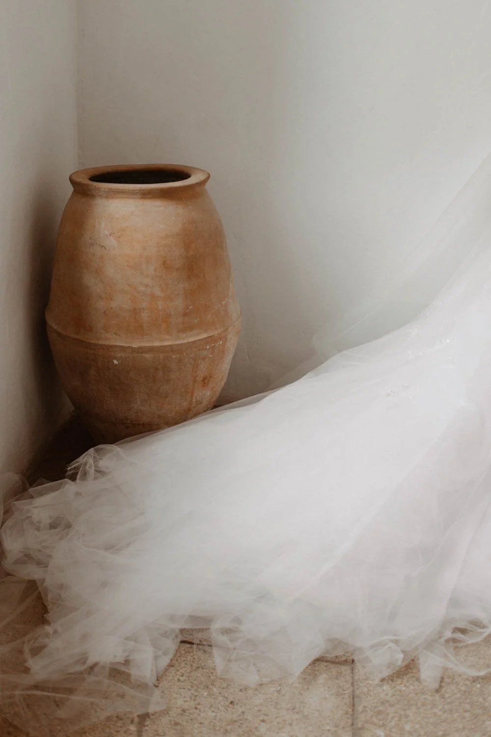 Grand pot en terre cuite beige placé dans un coin, recouvert d'un tissu blanc léger, posé sur un sol carrelé