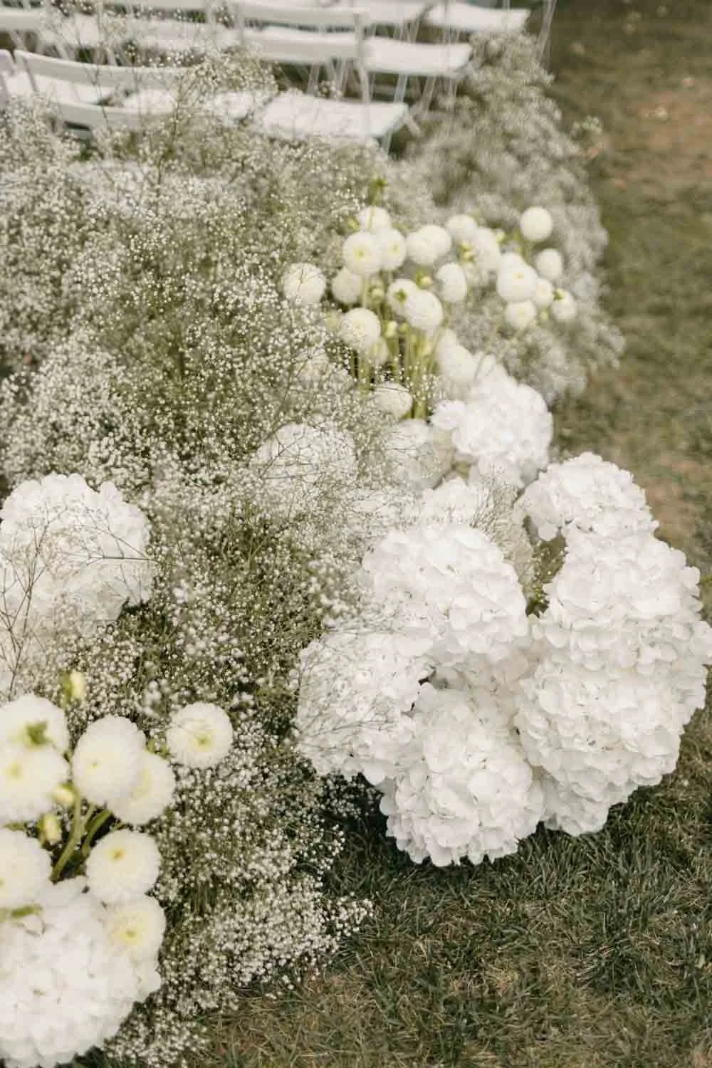 Arrangement floral blanc avec des fleurs de coton et de la gypsophile, installé sur le sol en extérieur.