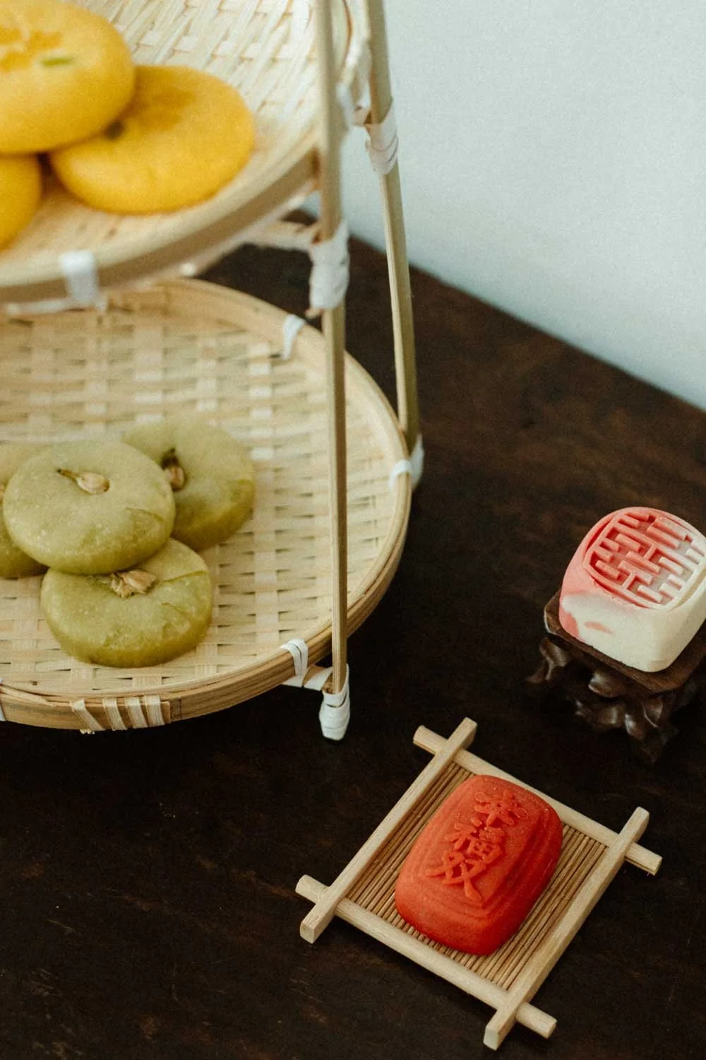 Gâteaux traditionnels chinois sur une étagère en bois, sous une structure en bambou, avec deux petits moulins à vent en bois à côté.