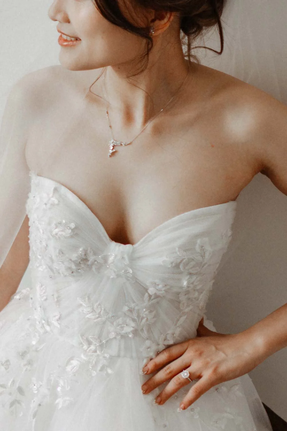 Une femme porte une robe de mariée blanche avec des détails floraux, un collier et une bague.