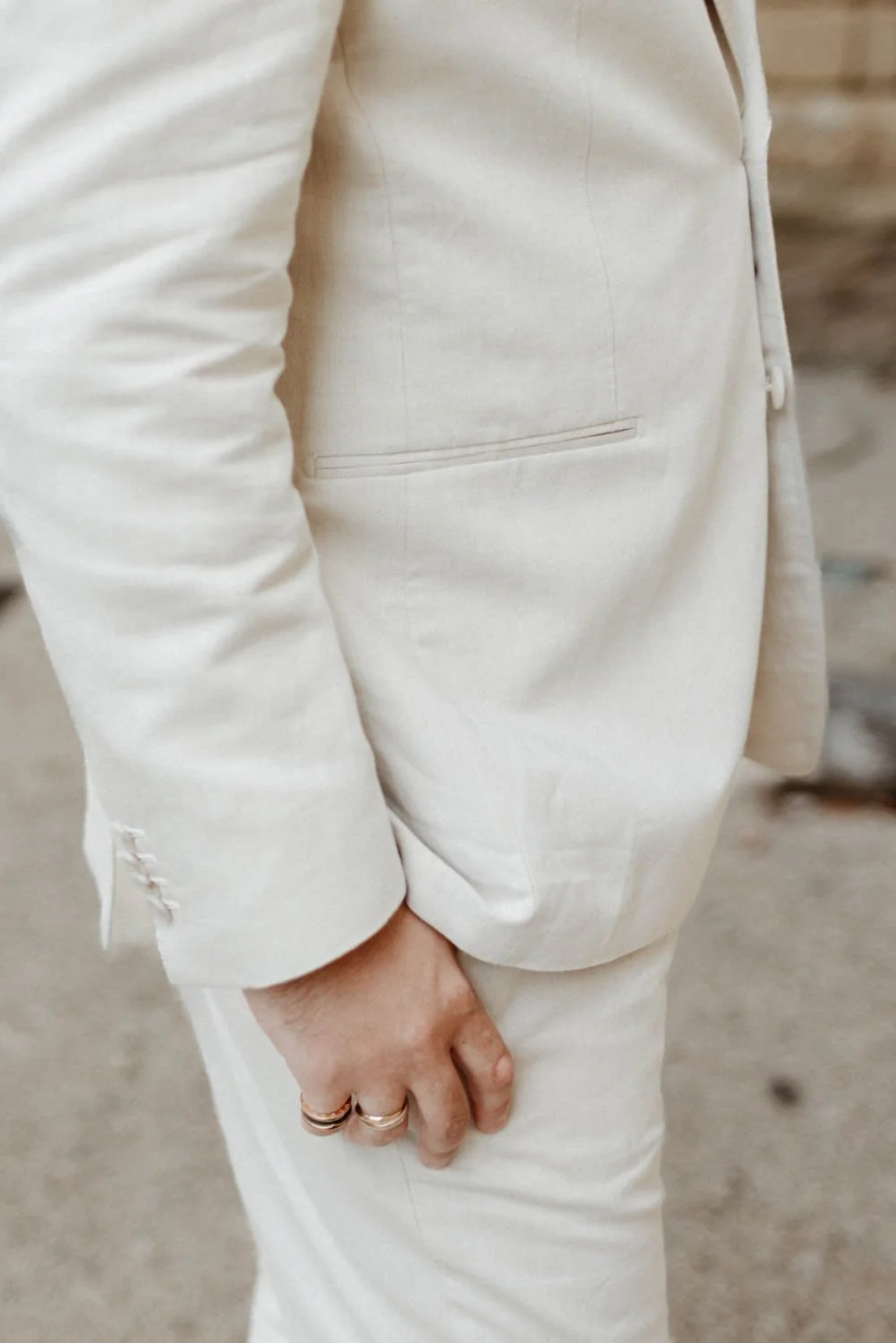 Veste et pantalon en tissu beige ou blanc cassé, avec poche sur la taille, main avec deux bagues.