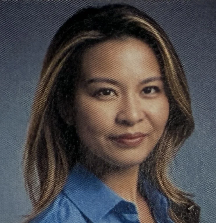 A woman with curly, shoulder-length hair smiling at the camera, wearing a red patterned top.