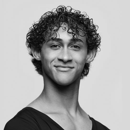 Black and white portrait of a young man with curly hair, smiling slightly, wearing a dark shirt.