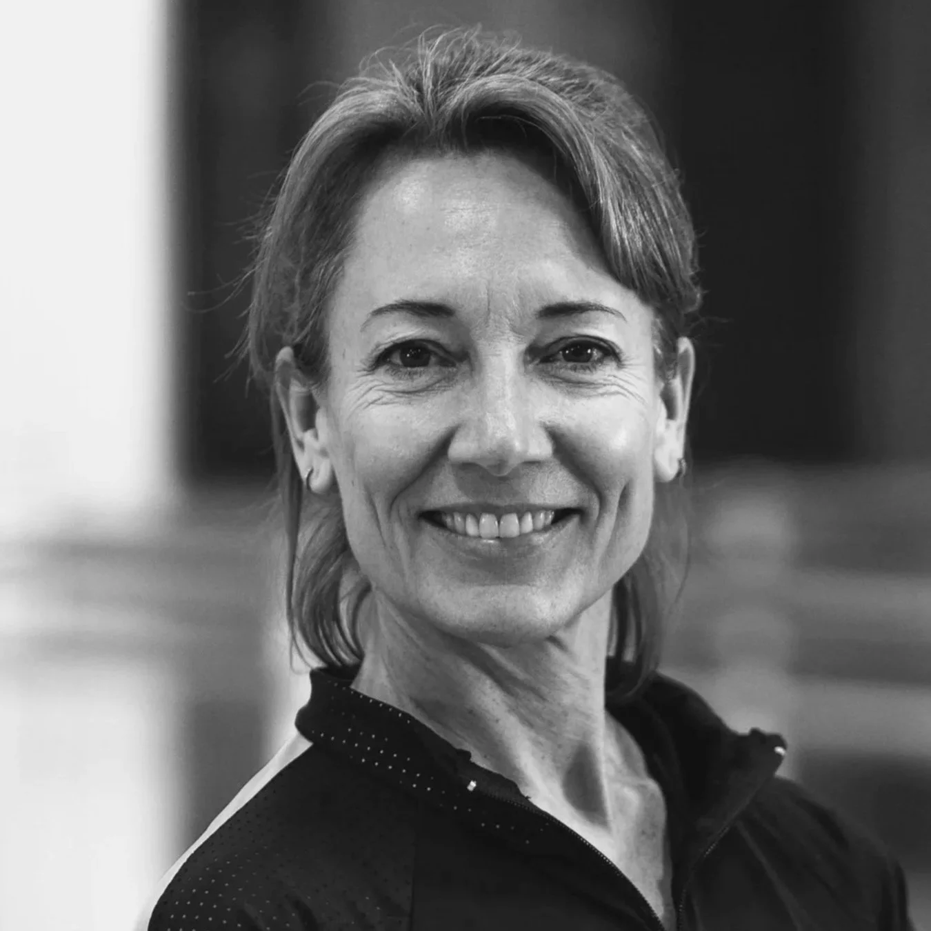 Black and white photo of a smiling middle-aged woman with short hair, wearing a sporty zip-up top.
