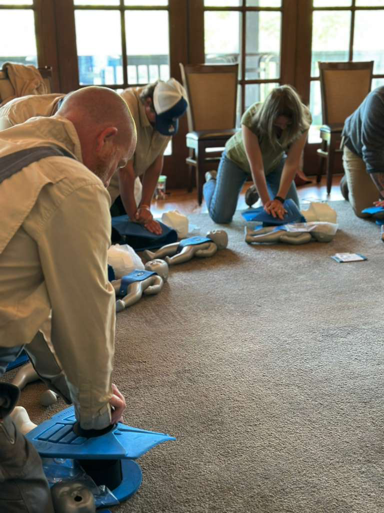 People participating in a CPR training session indoors, practicing on CPR mannequins on the carpeted floor.