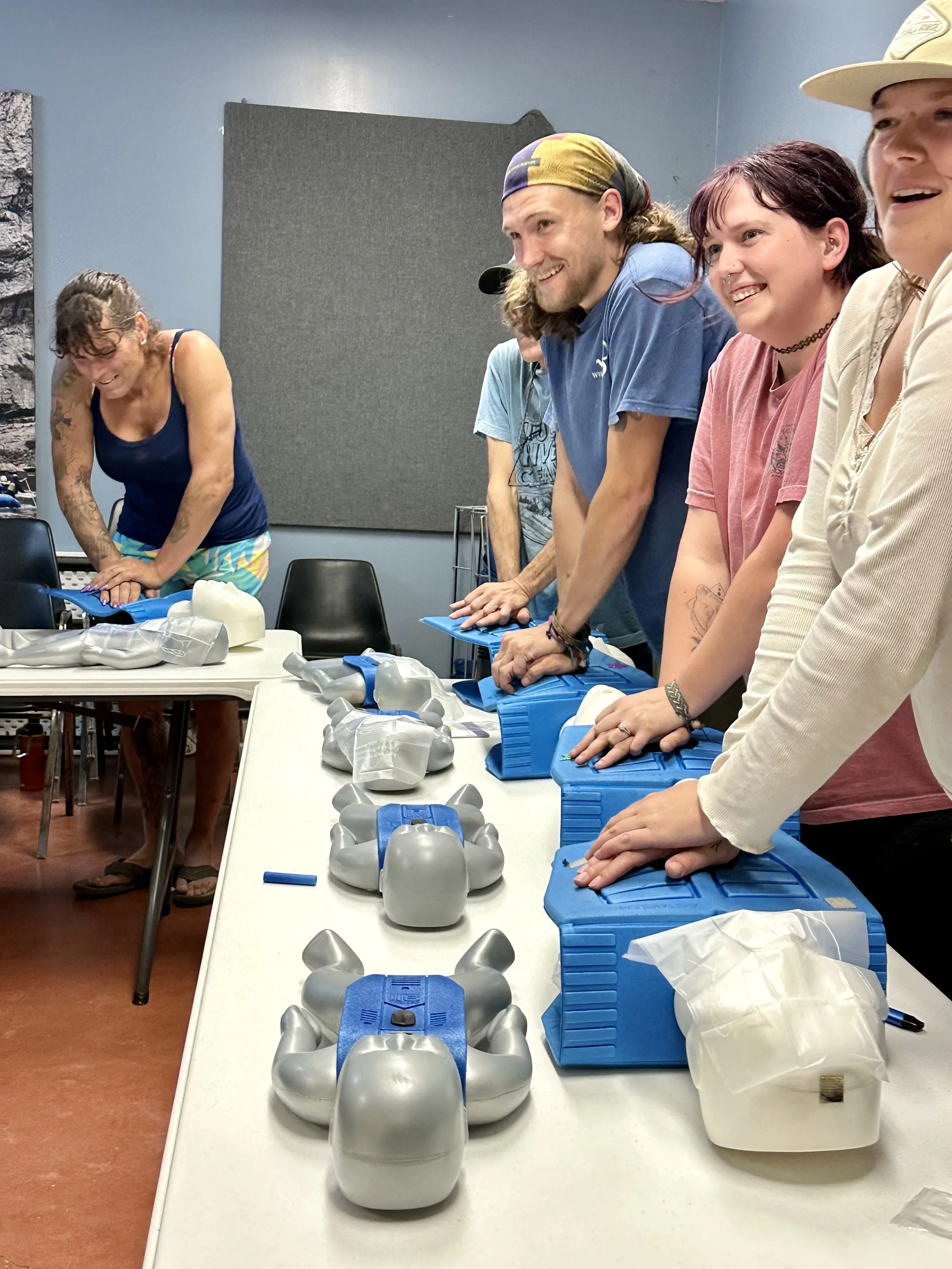 Group of people standing at a table with plastic molds and blue toolboxes, smiling and leaning forward in a workshop or classroom setting.