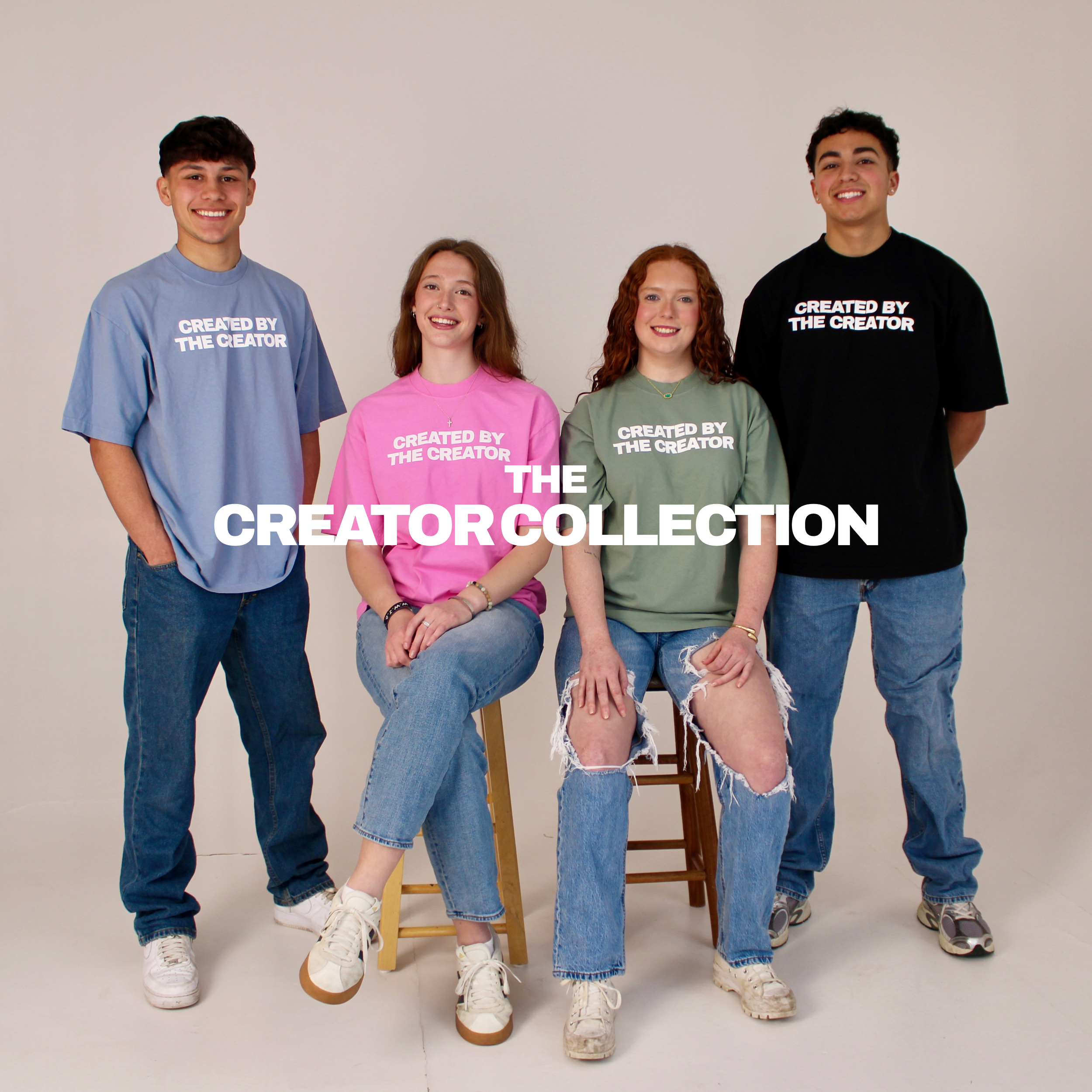 Five young people standing against a plain background, wearing colorful T-shirts that say 'Created by the Creator'. Two are sitting on a wooden chair. They are smiling and looking at the camera.