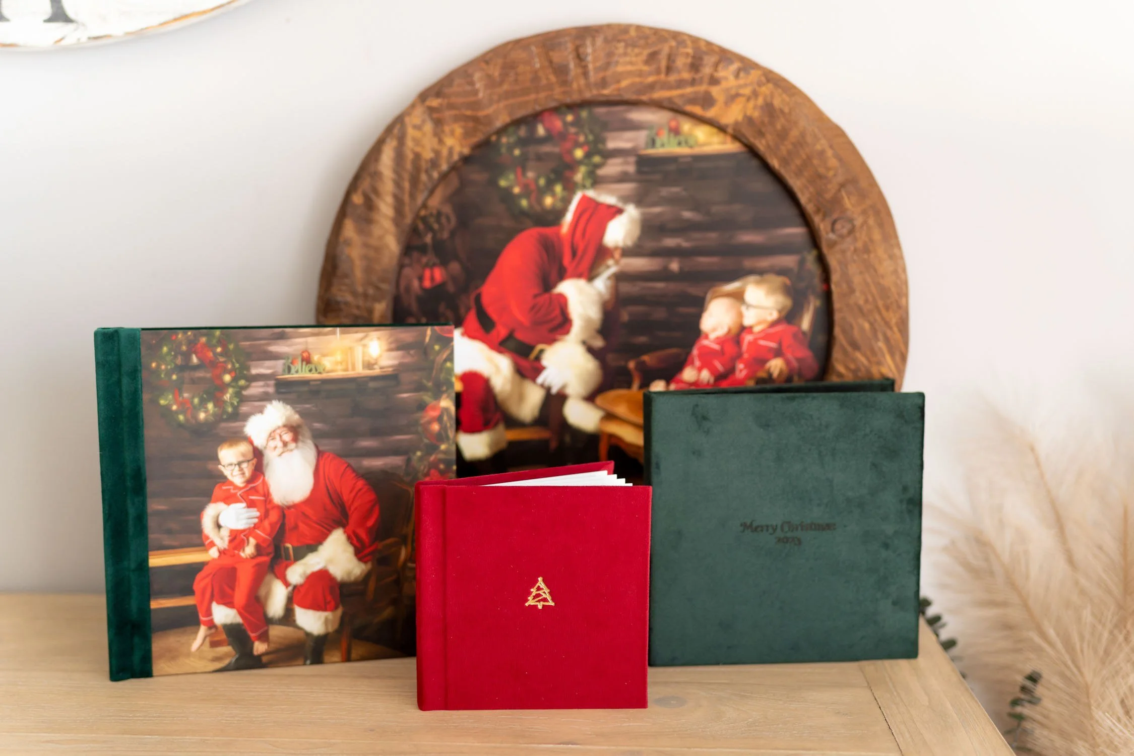 Collection of custom Santa portrait products including albums, framed artwork, and a round wooden photo display.
