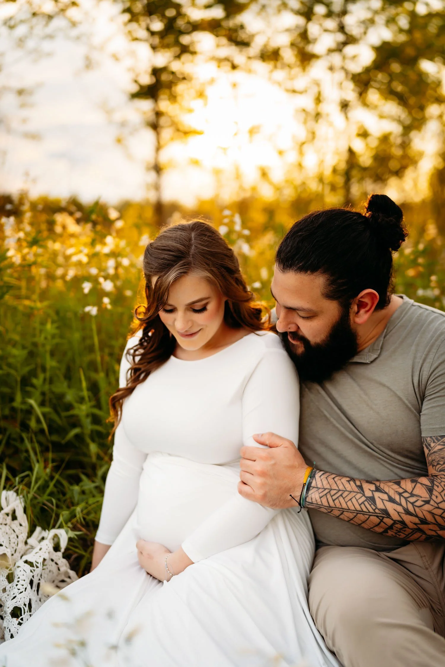 Expecting couple sitting together outdoors with the father leaning toward the mother’s baby bump.