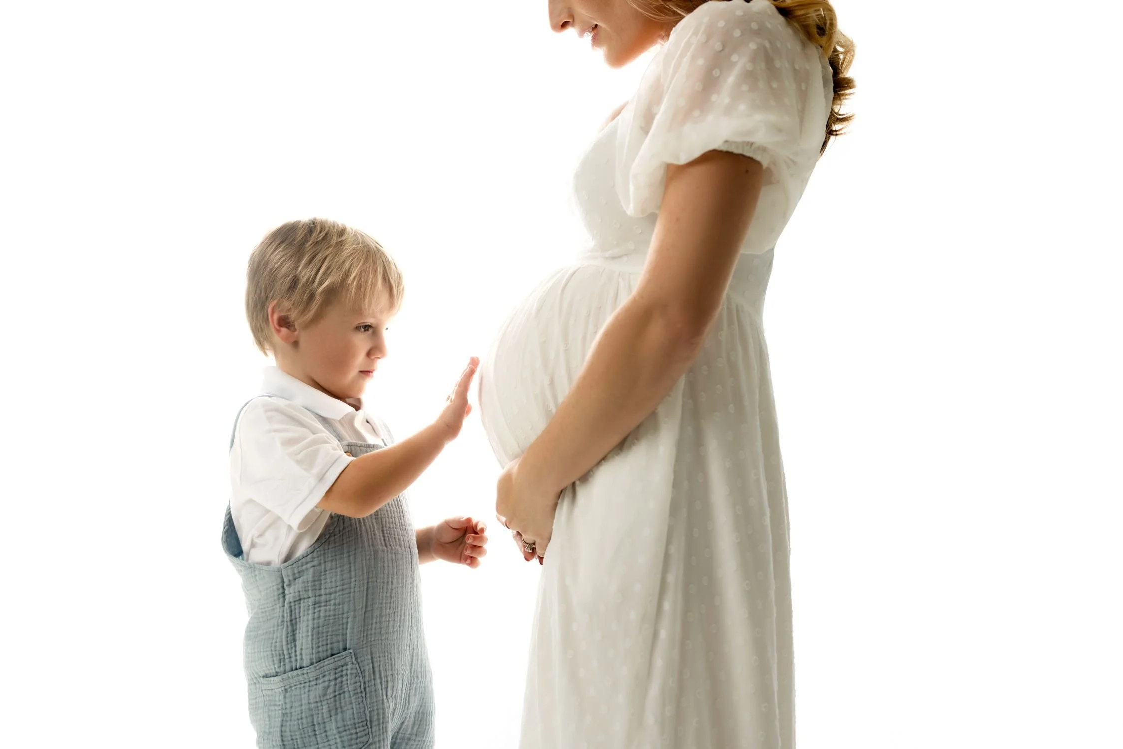 Young boy reaching toward his mother’s baby bump during a maternity session in St. Louis