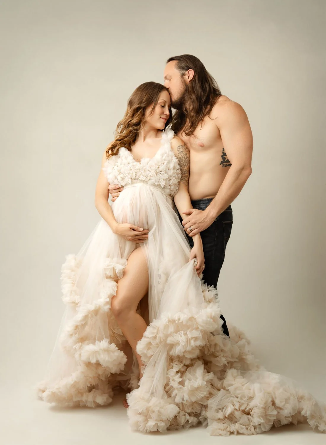 pregnant woman in a dramatic cream ruffled gown posing with her partner during an intimate, editorial-style studio maternity portrait session in St. Louis.