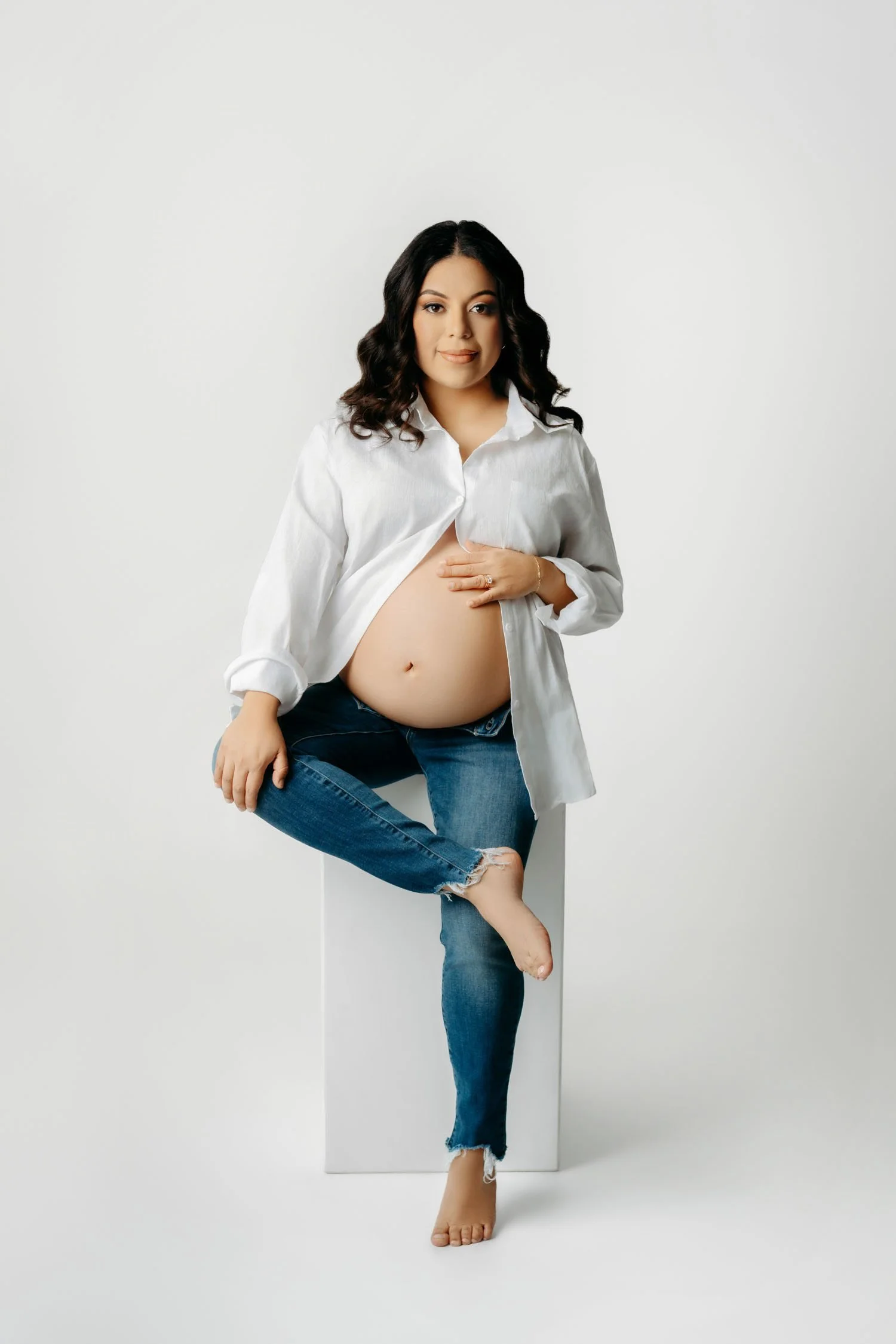Pregnant woman in jeans and an open white shirt posing casually during a St. Louis maternity session.