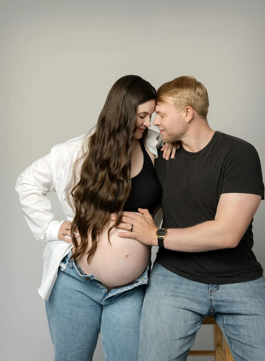 Expecting couple sitting together and sharing a playful moment during a casual maternity portrait.