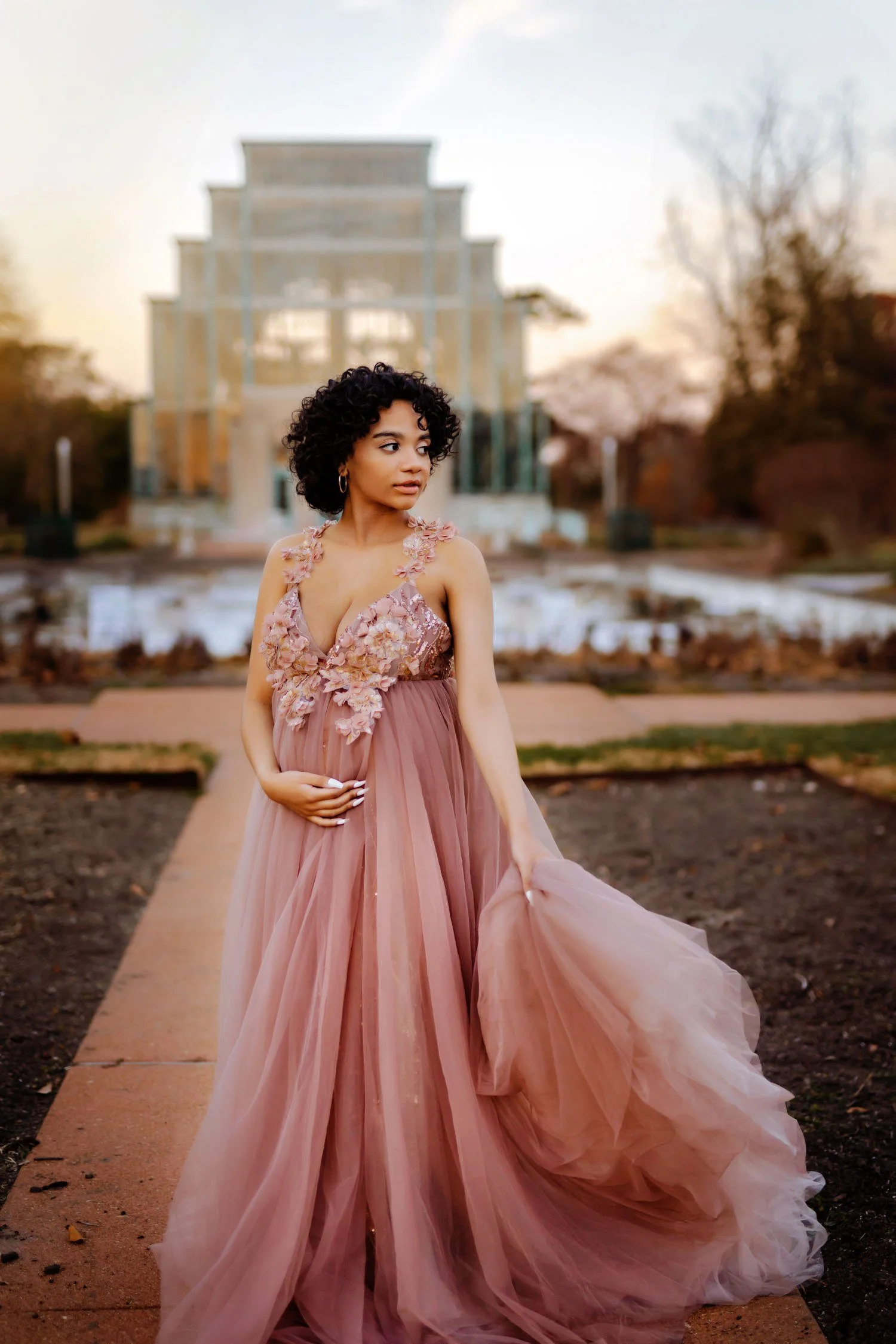 Pregnant woman in a flowing blush gown posing outdoors near a St. Louis landmark The Jewel Box.