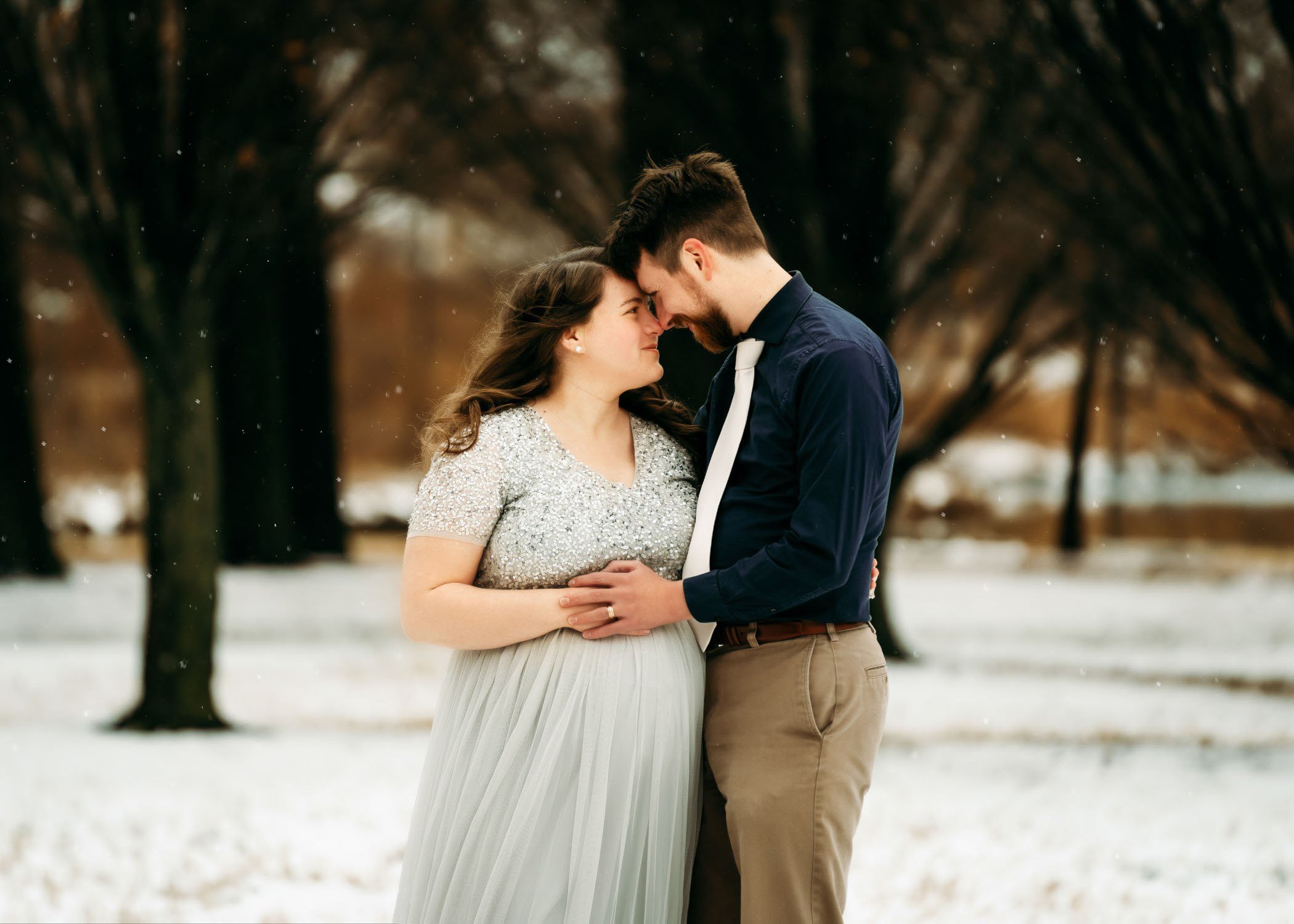 Pregnant couple embracing outdoors in the snow during a winter maternity photography session.