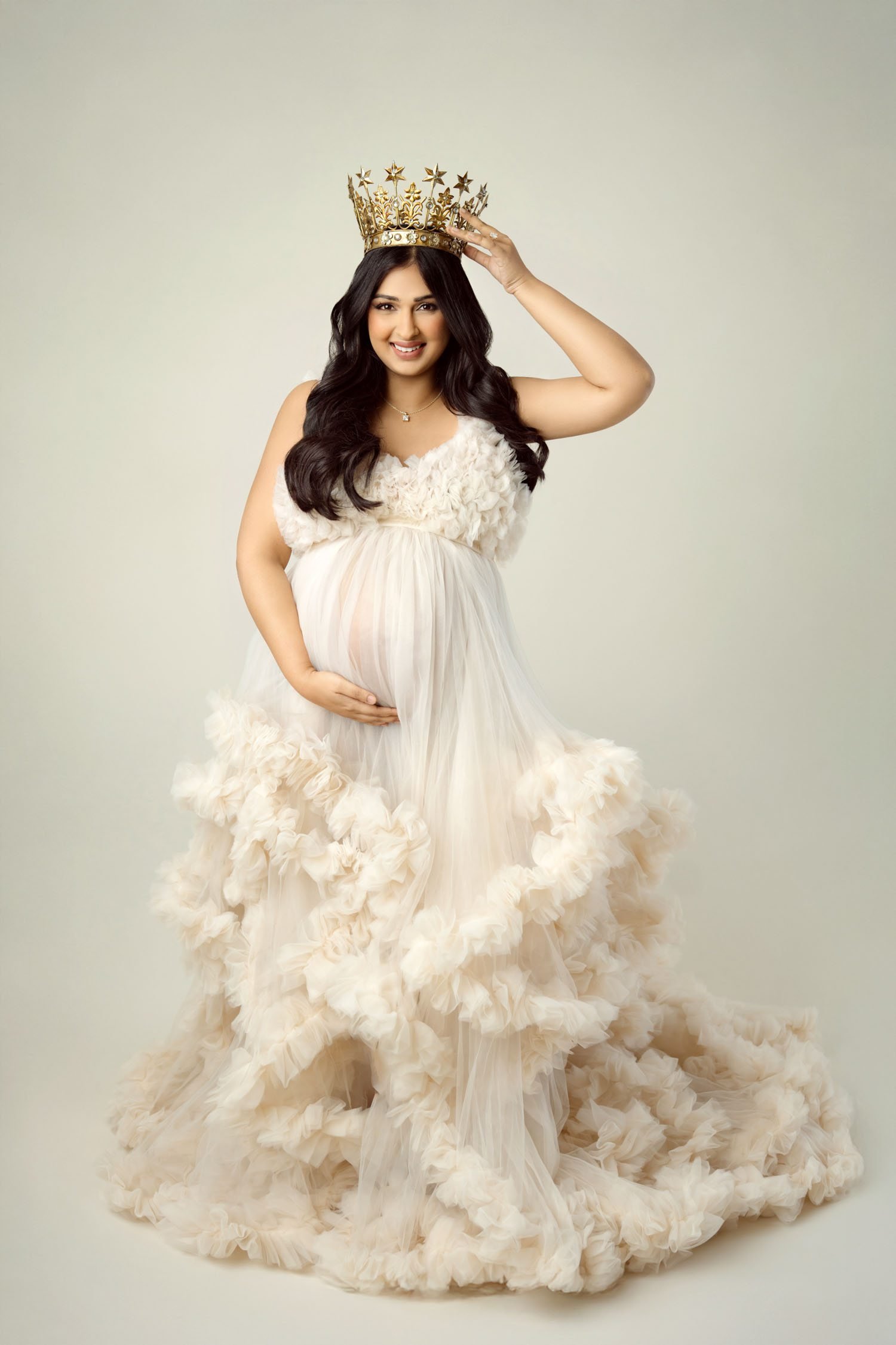 Pregnant woman in a cream floral maternity gown posing in a studio portrait.