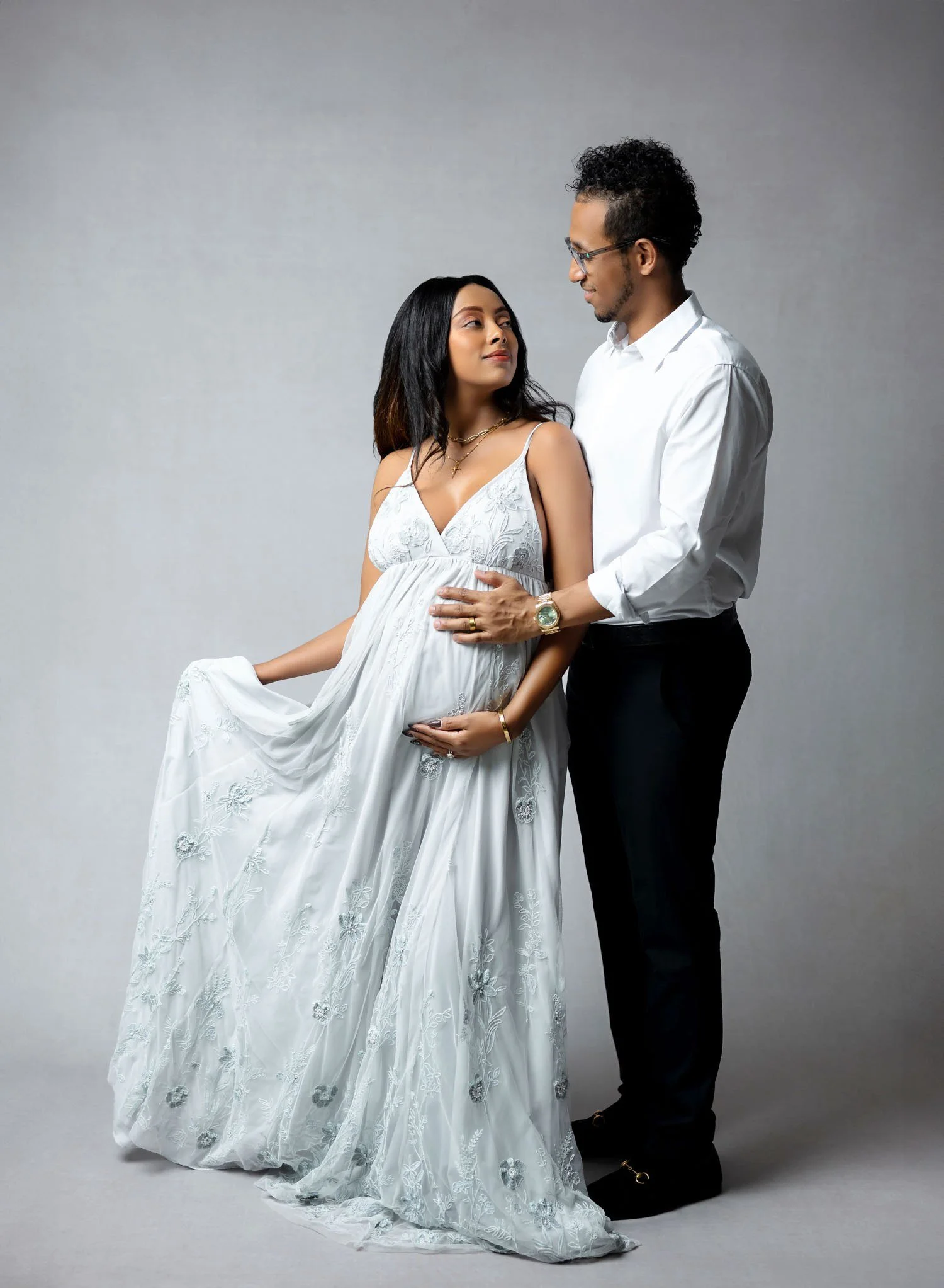 Pregnant couple standing together in an elegant maternity portrait with the mother wearing a light blue gown.
