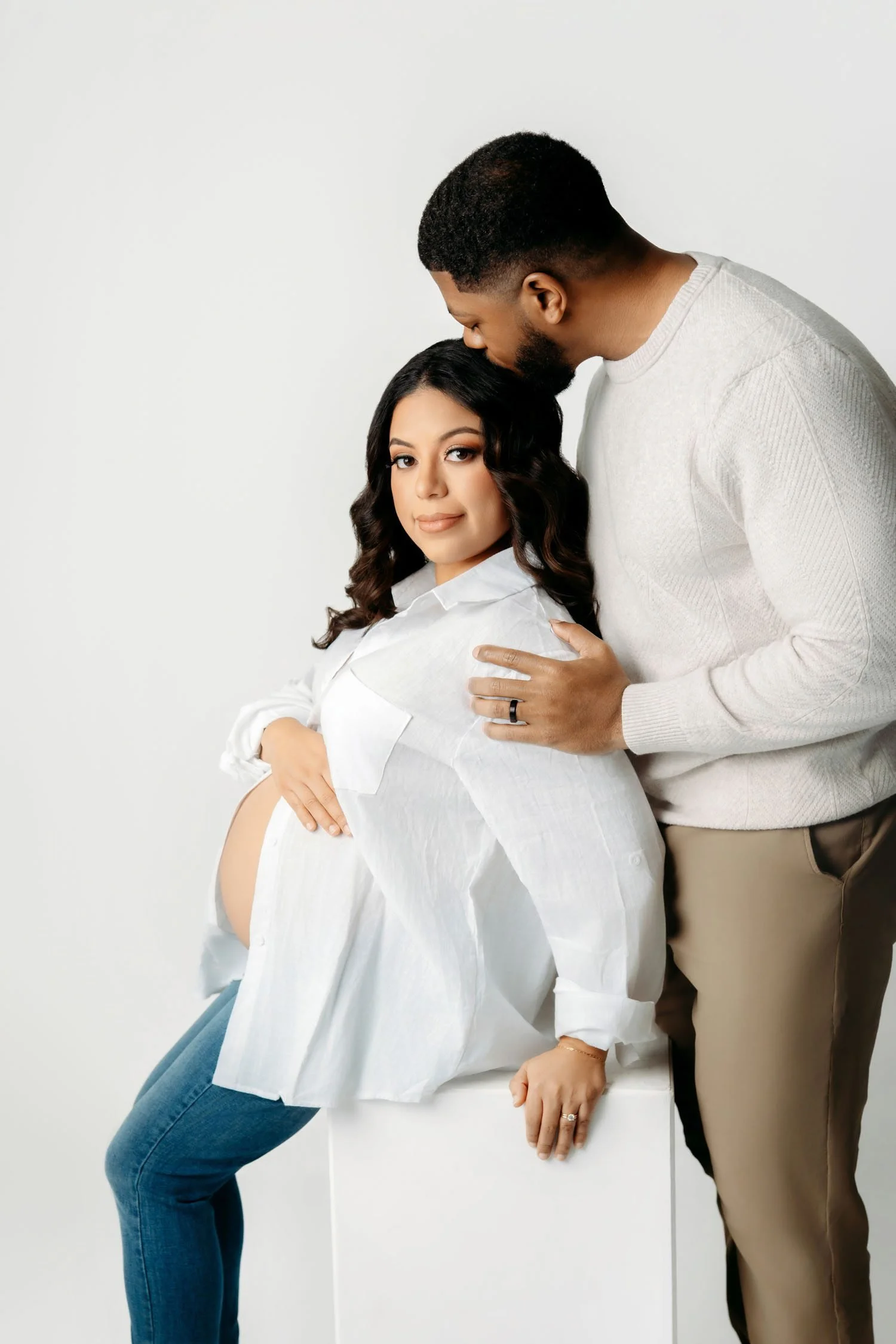 Expecting couple sharing a quiet moment during a seated studio maternity portrait.