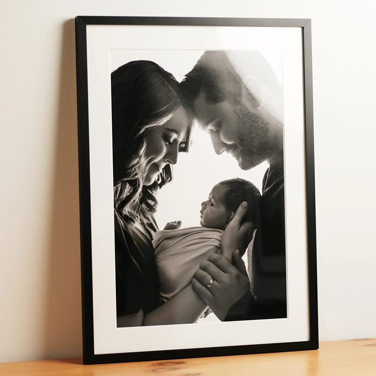 Framed black and white newborn portrait of parents holding their baby.