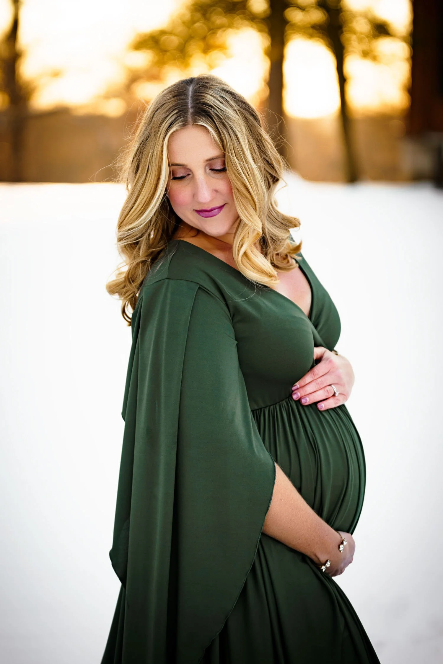 Expecting mother in a flowing green gown posing outdoors at sunset during a St. Louis maternity session.