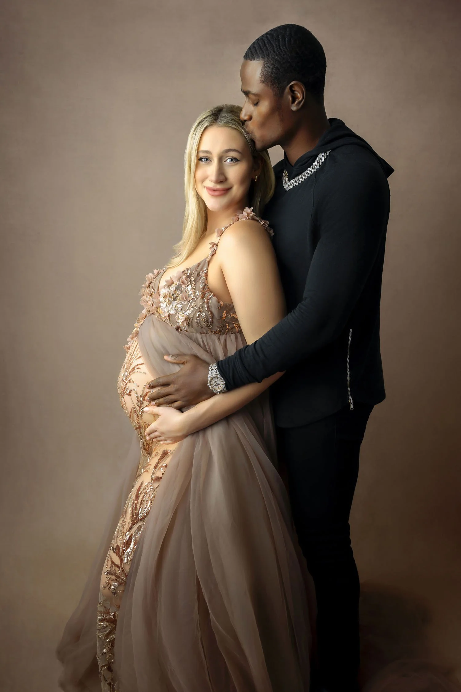 Expecting couple embracing in an elegant studio maternity portrait.