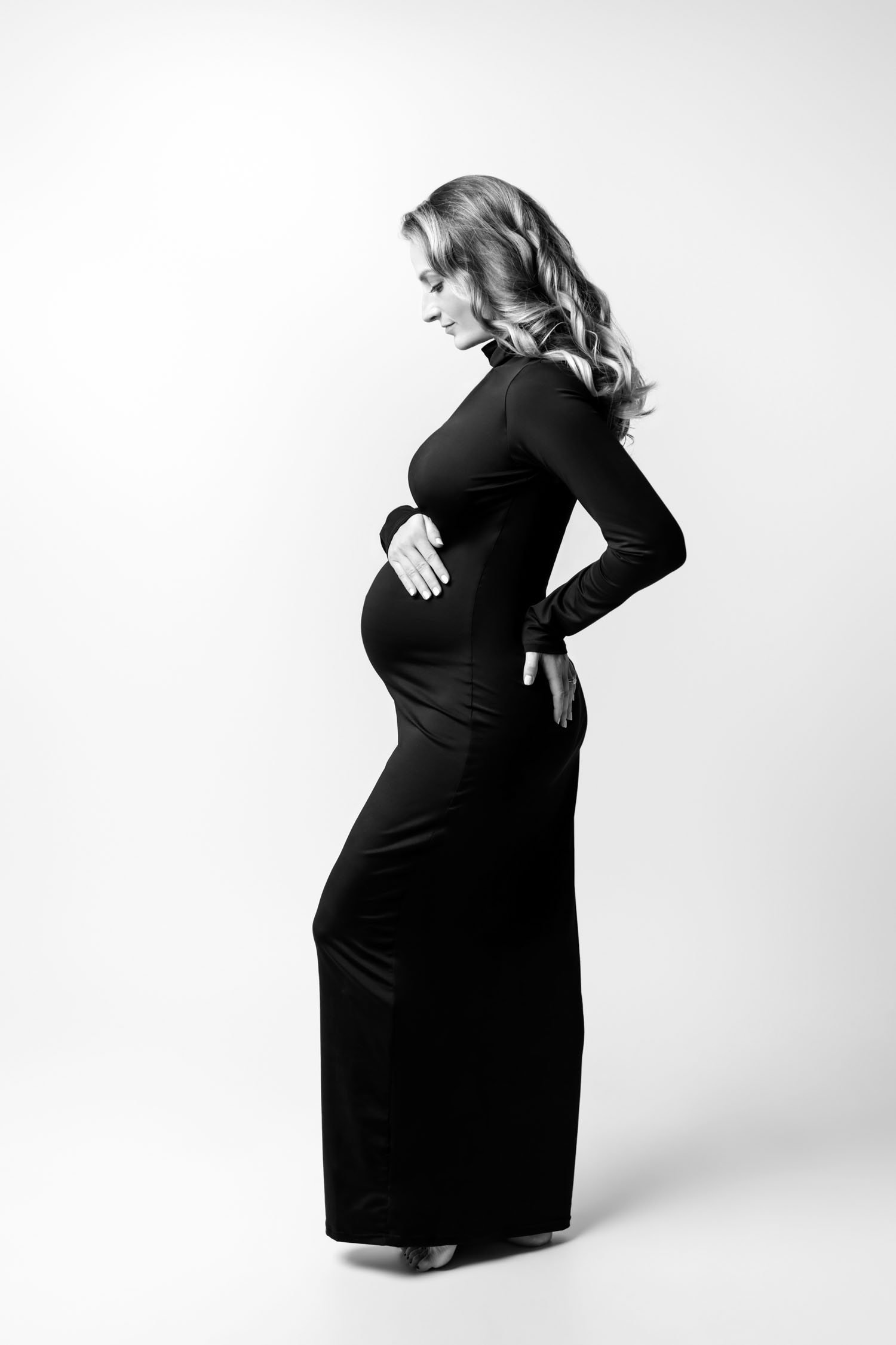 Black and white profile portrait of a pregnant woman in a fitted black maternity gown.