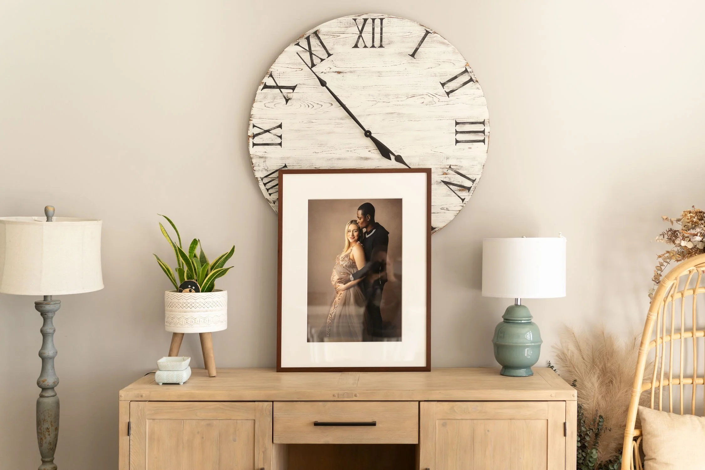 Framed maternity photograph displayed beneath a large wall clock in a styled room.