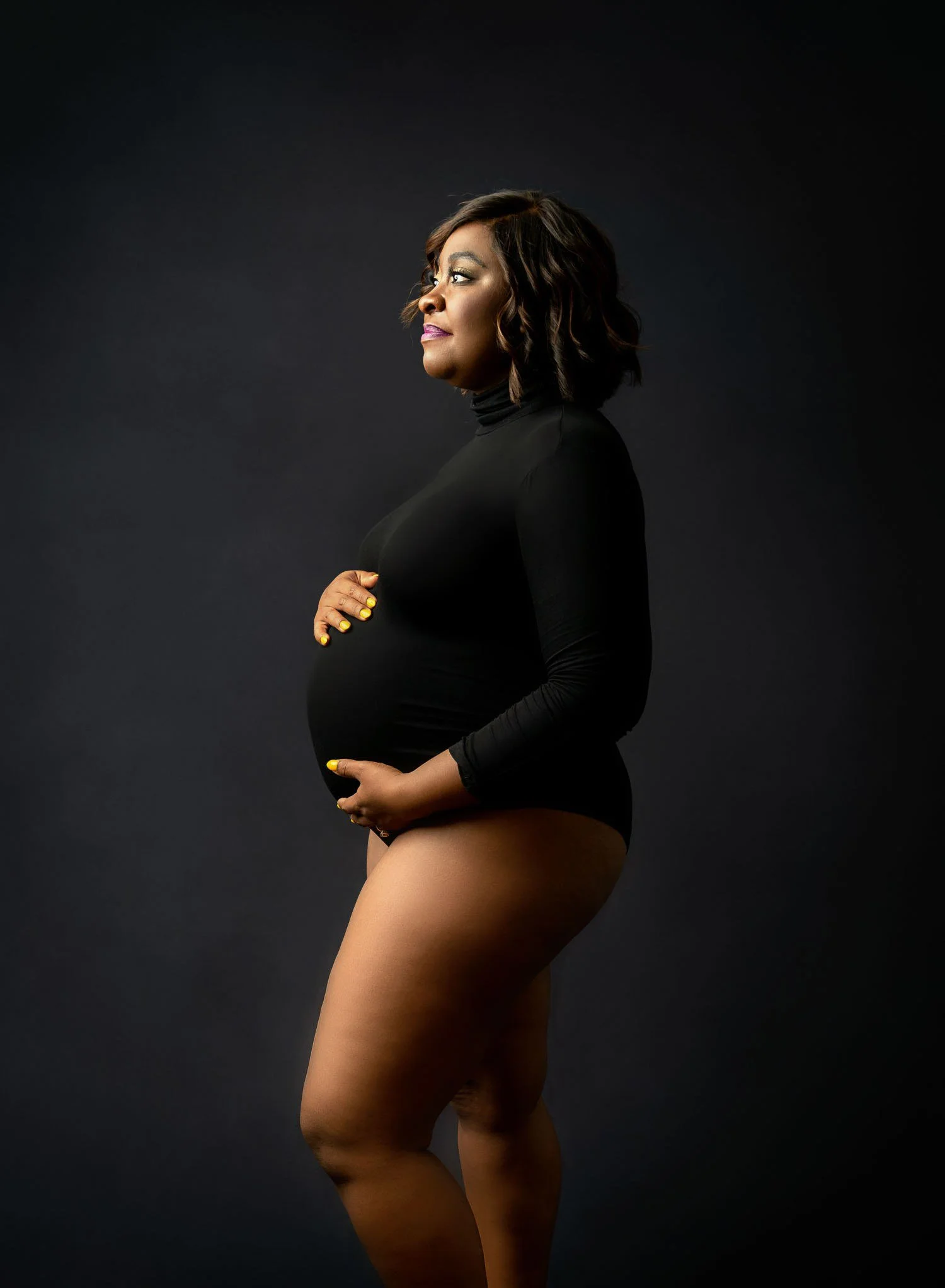 Pregnant woman in a black bodysuit posing in profile during a studio maternity session in St. Louis.