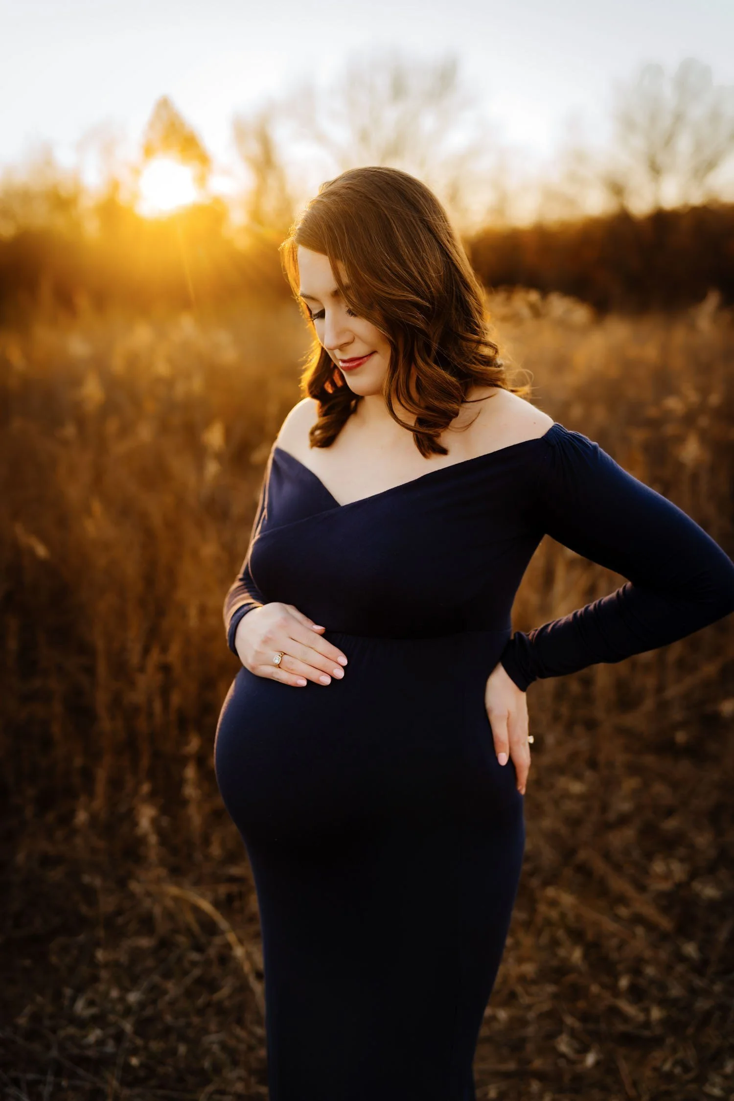 Expecting mother in a fitted navy maternity gown posing outdoors at sunset in St. Louis.