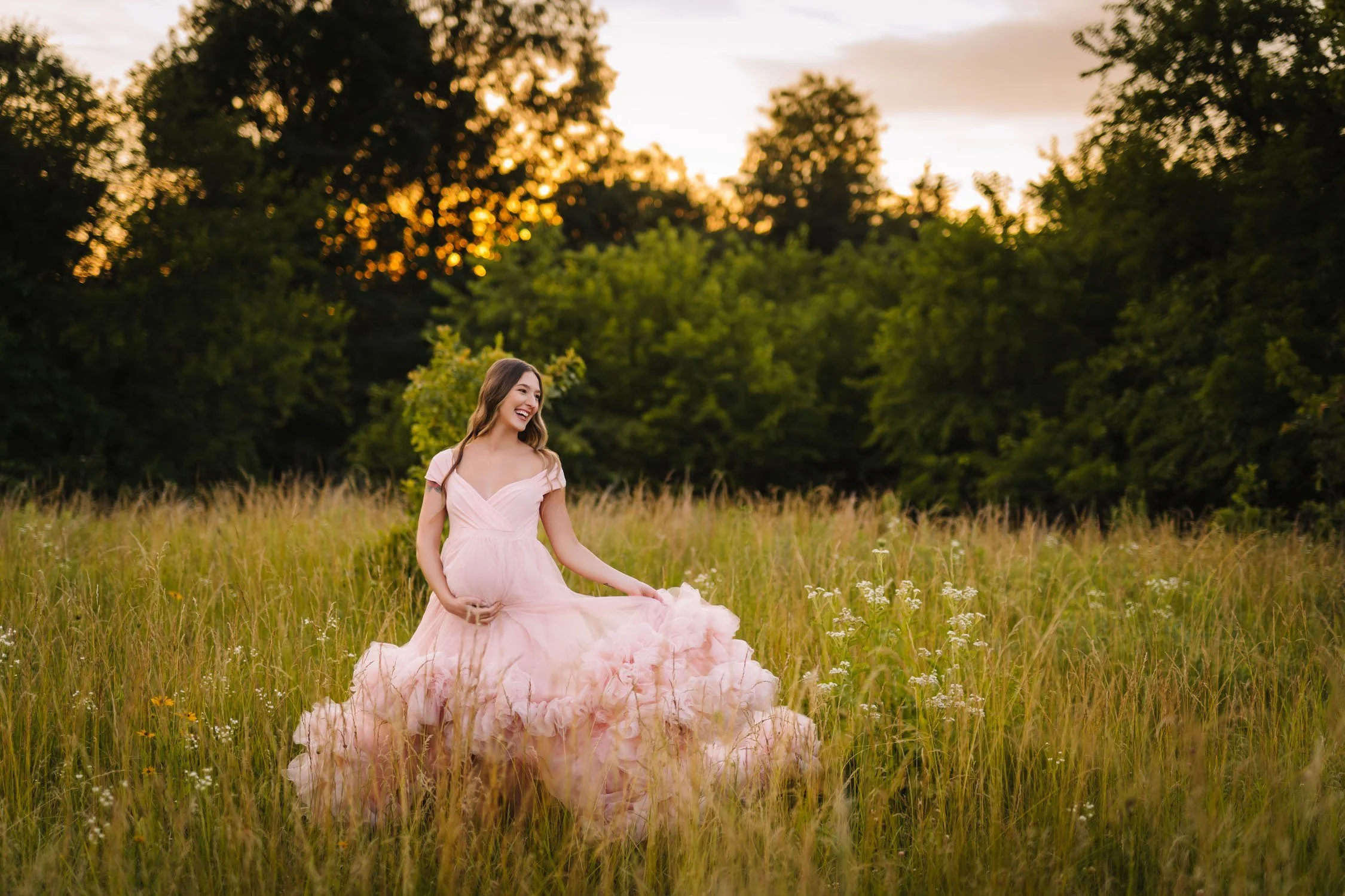 Pregnant woman in a blush gown sitting in a wildflower field during a St. Louis maternity photography session at Towne Park.
