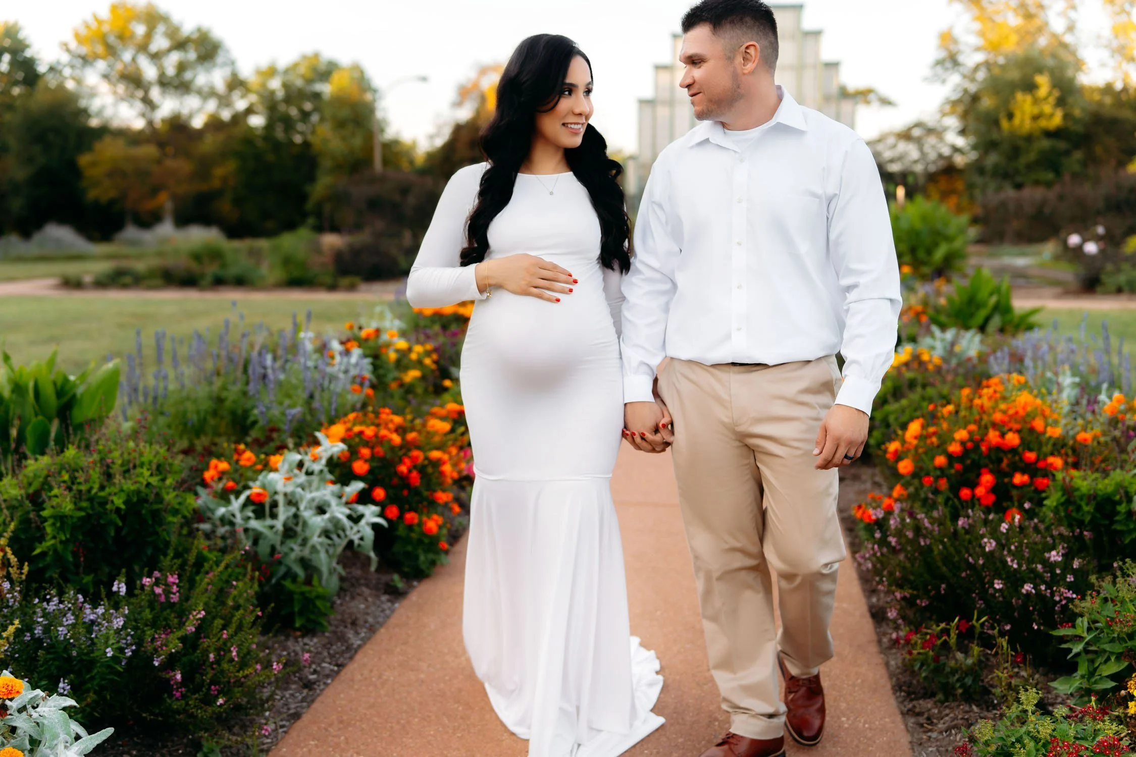 Expecting couple walking together through colorful gardens during an outdoor maternity portrait.