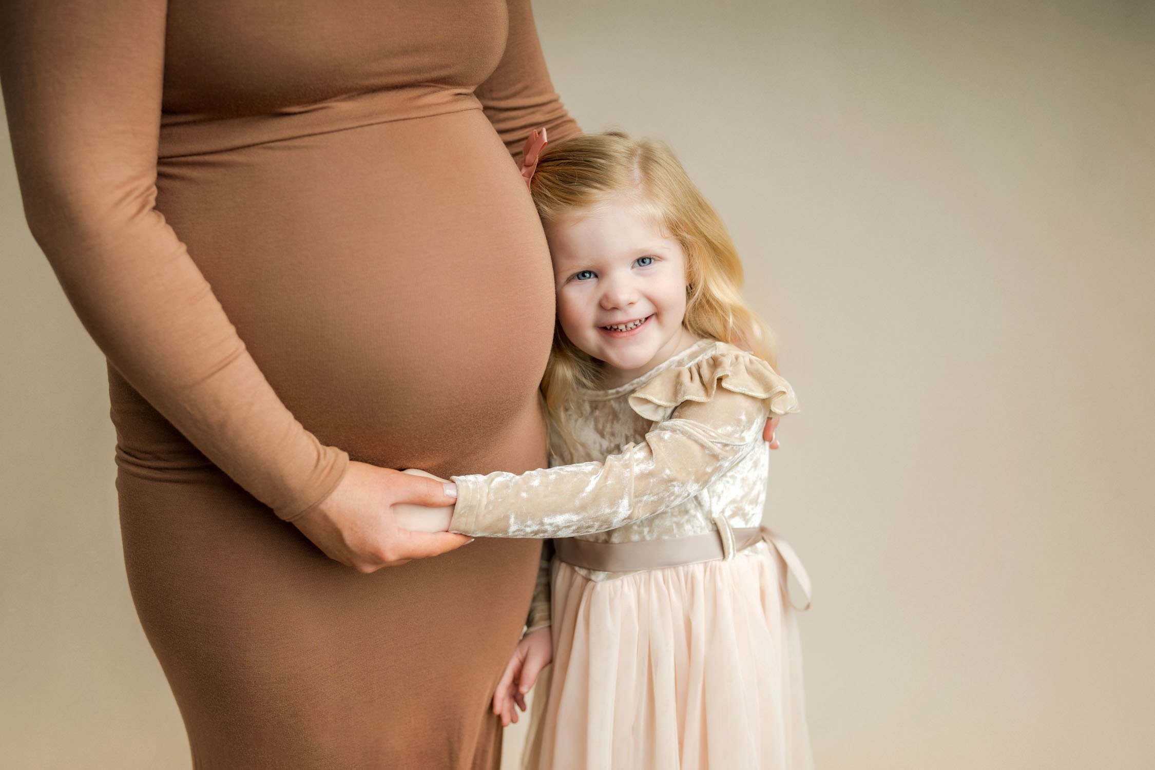 Young girl hugging her mother’s baby bump during a maternity portrait.