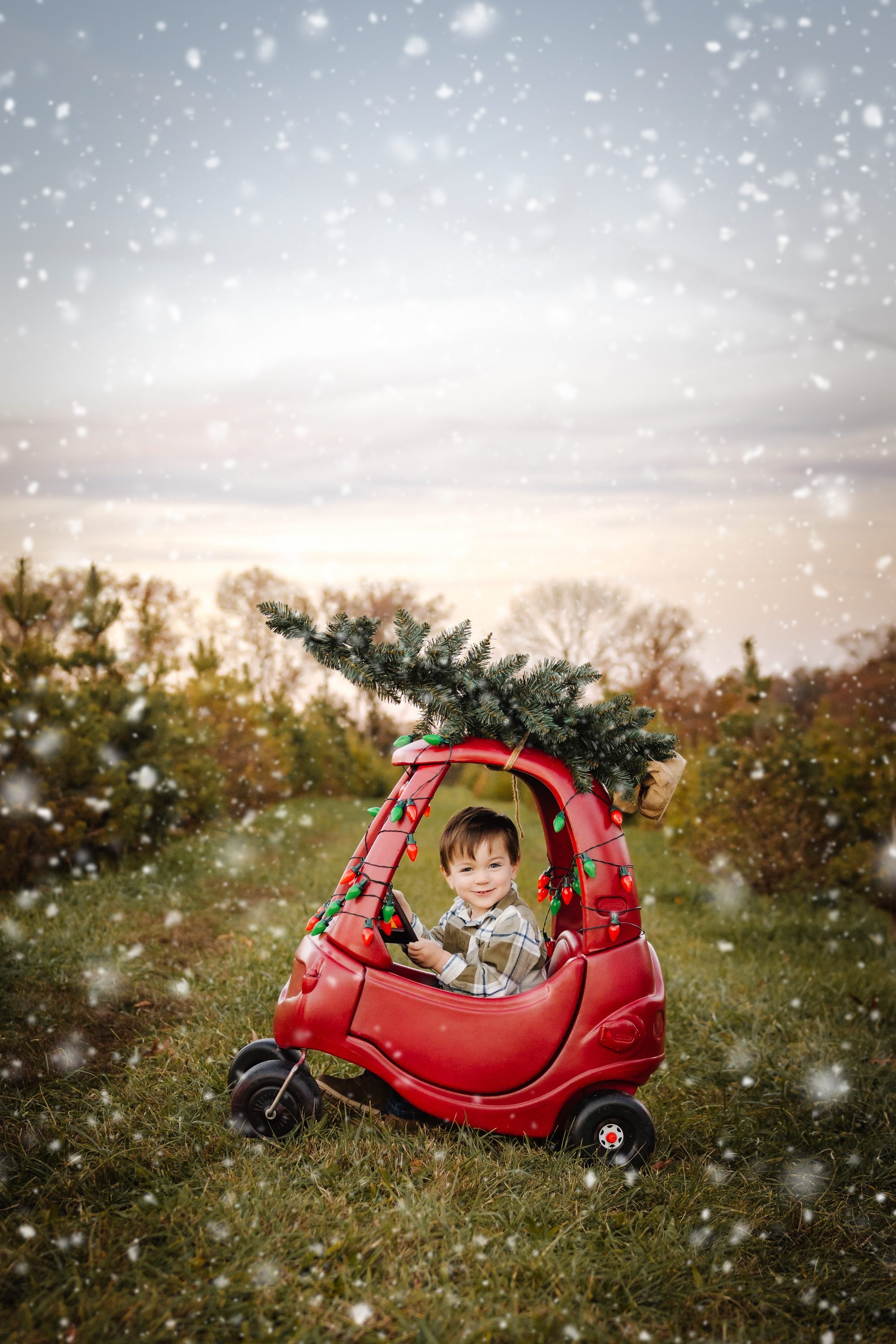 Young child sitting in a red toy car during an outdoor Christmas tree farm photo session in Wright City, Missouri.