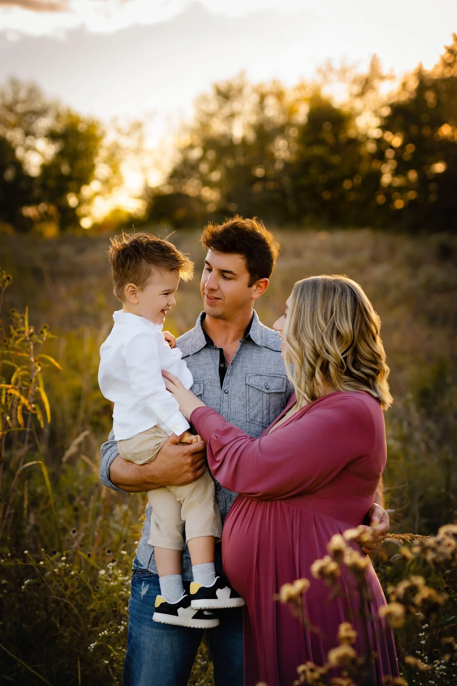 Expecting parents with their young son during a family maternity session at sunset.