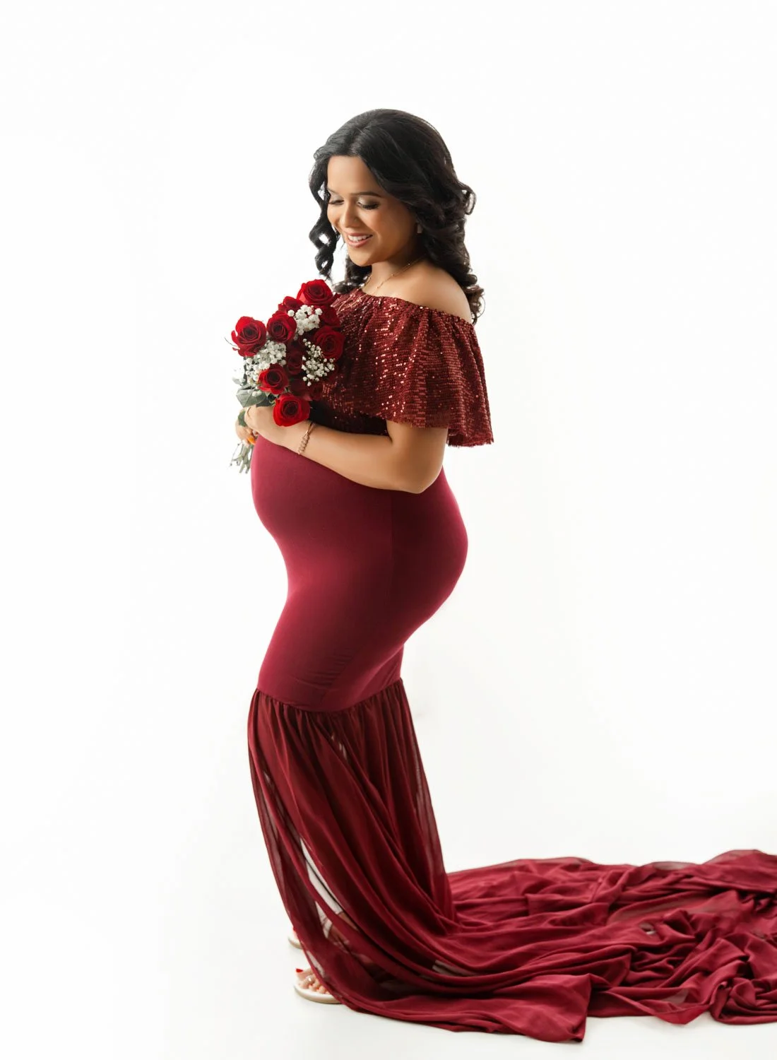 Pregnant woman in a fitted red gown holding a bouquet during a St. Louis maternity photography session.
