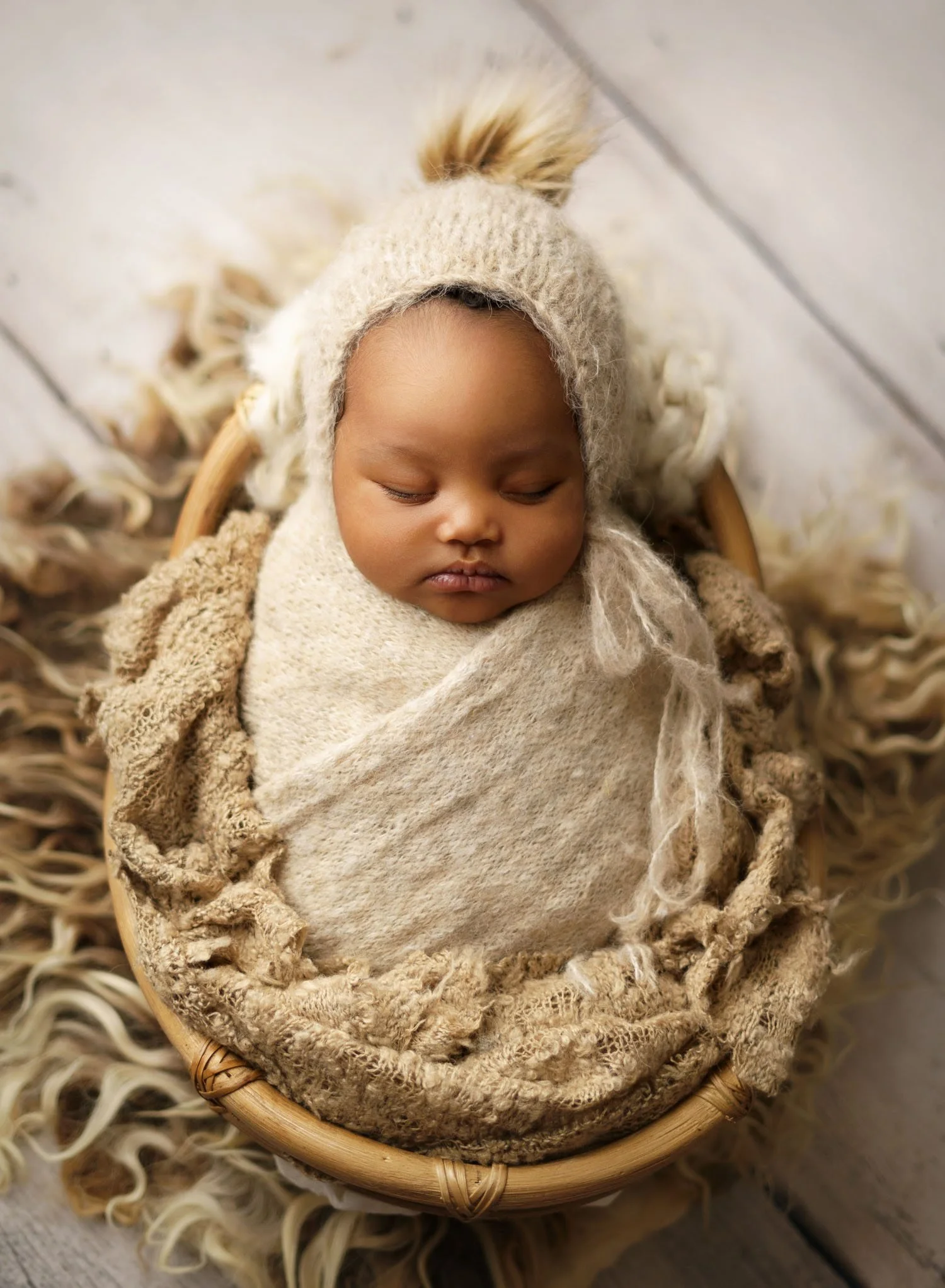 A newborn baby sleeps in a cream knit swaddle and matching bonnet in a wooden basket thanks to lactation consultants in st louis