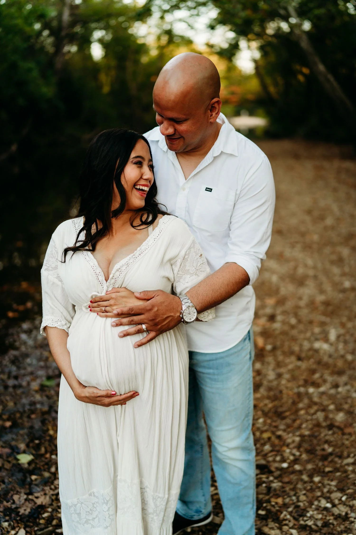 Expecting couple embracing outdoors with their hands resting on the baby bump.