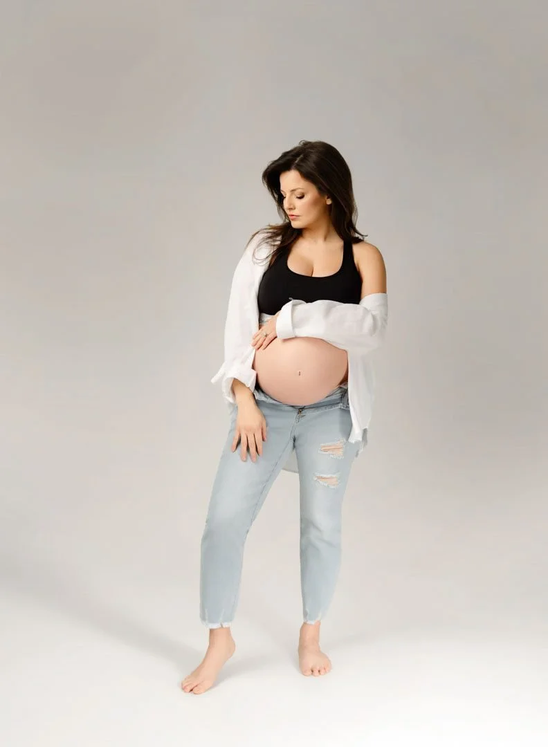 Casual maternity portrait of an expecting mother in jeans and a white top in a St. Louis photography studio.