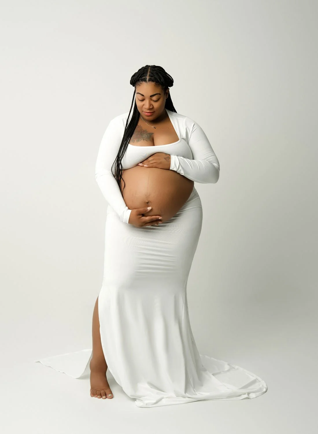 Expecting mother in a fitted white maternity gown cradling her baby bump.